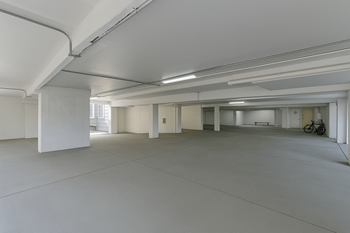 A large, empty, white room with a bicycle in the background.